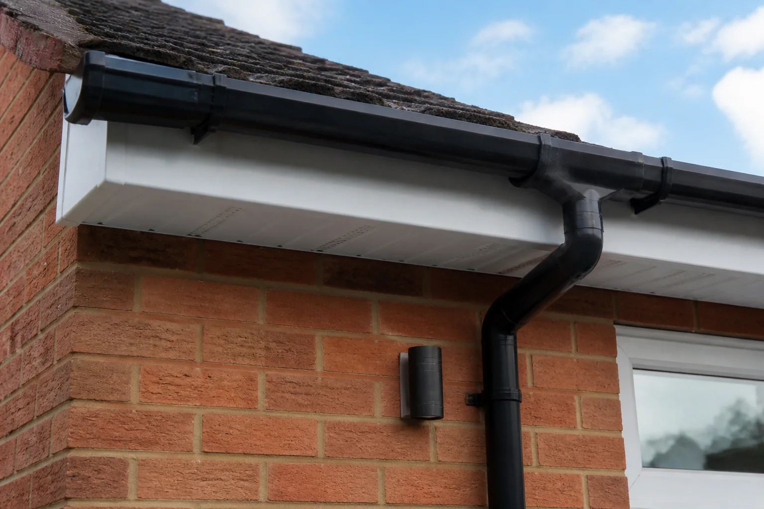 Illustrative close view of a coordinated British roofline, gutter, soffit and warm exterior lighting detail; not a completed Zamax project